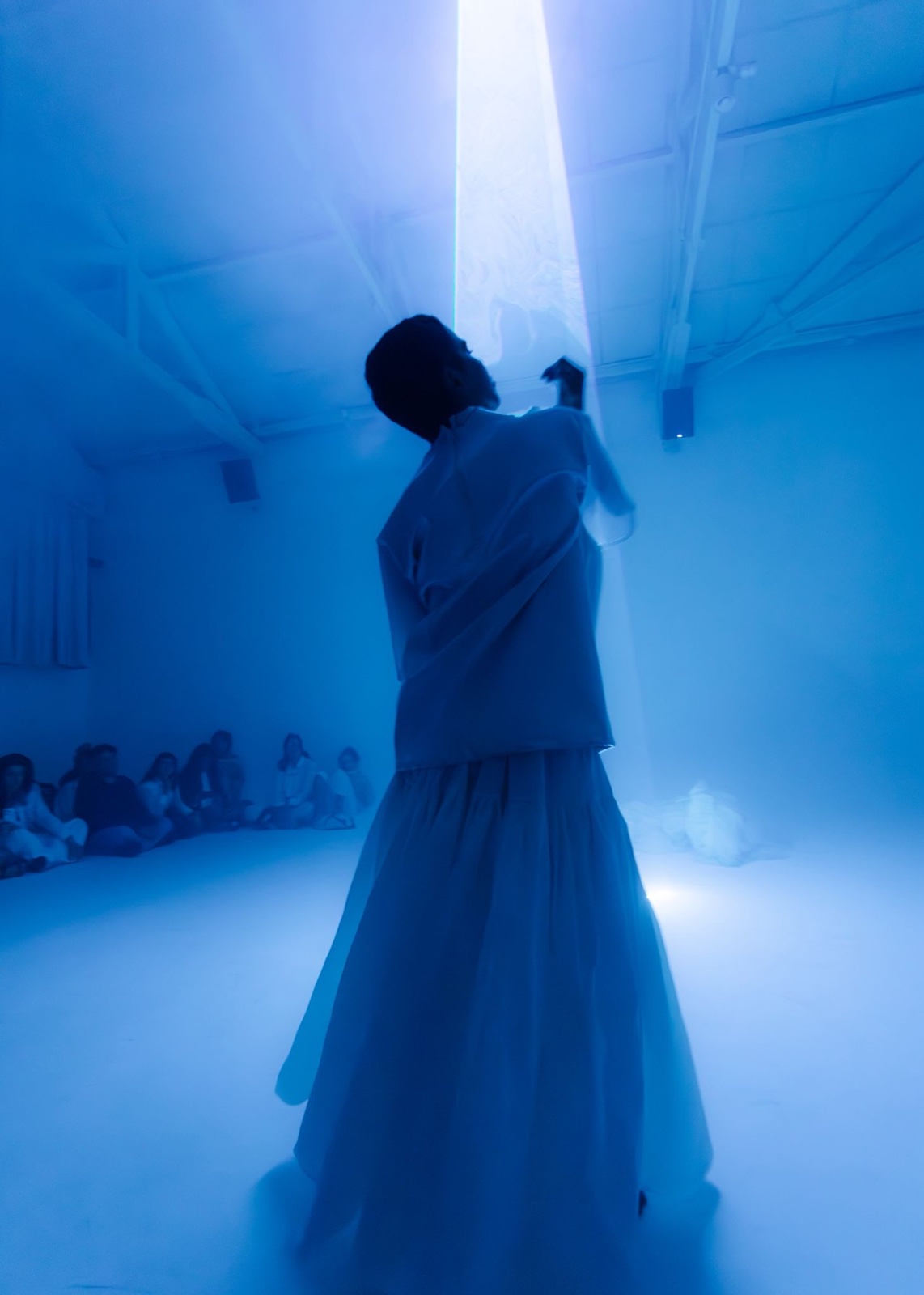Performer silhouetted in blue mist with audience seated around